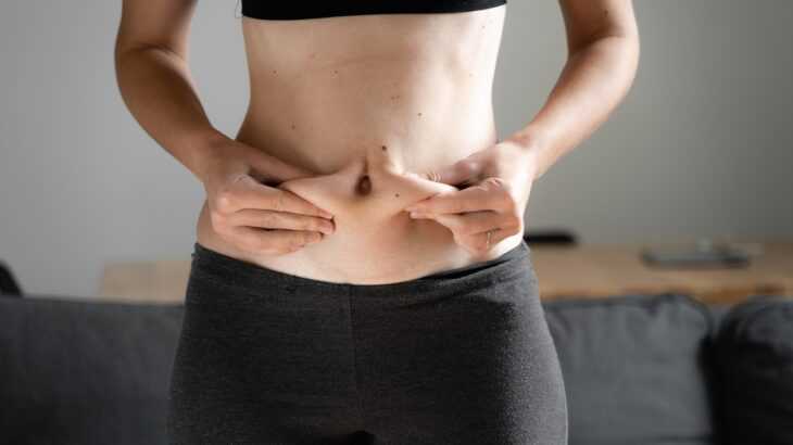 cintura de uma mulher apertando a sua gordura abdominal