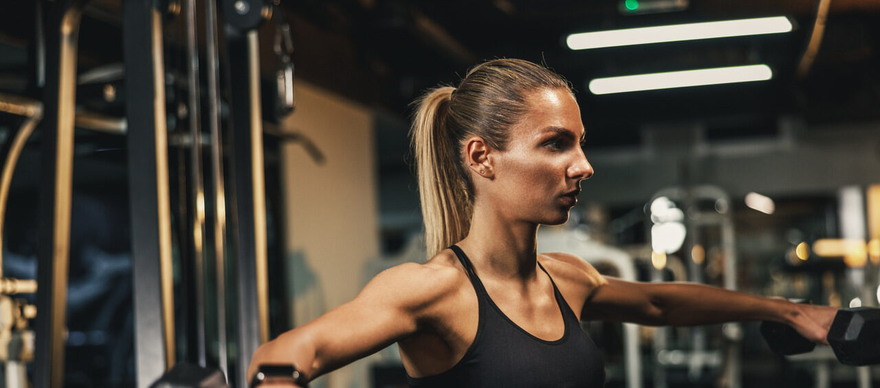 mulher fazendo o exercício elevação lateral na academia