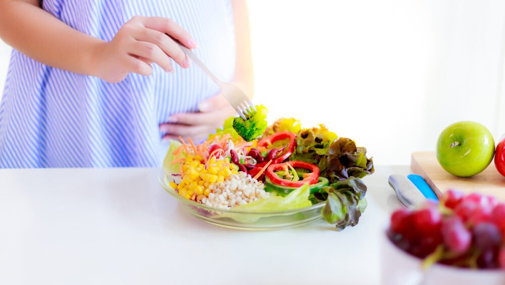 Prato com alimentos saudáveis com uma barriga de gestante ao fundo