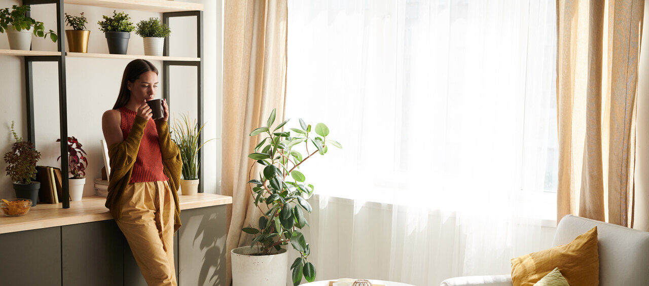 mulher na sala de estar encostada na bancada e bebendo uma xícara de chá