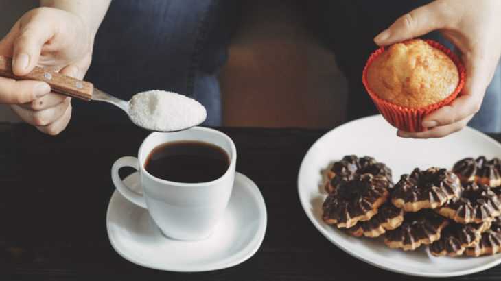 Mãos femininas colocando açúcar no café e segurando um muffin doce