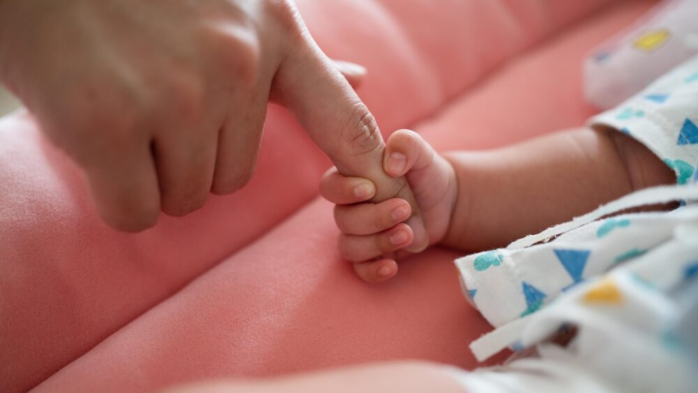 Mão de bebê recém-nascido segurando o dedo de uma mão adulta