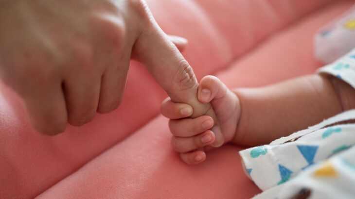 Mão de bebê recém-nascido segurando o dedo de uma mão adulta
