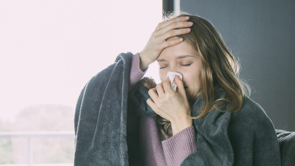 Mulher resfriada e com cobertas assoando o nariz