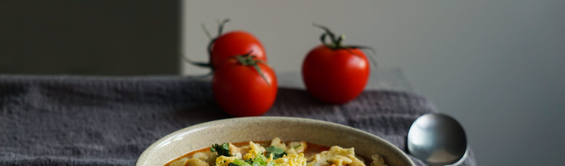 prato com sopa de macarrão e carne. Ao lado, dois tomates e uma colher