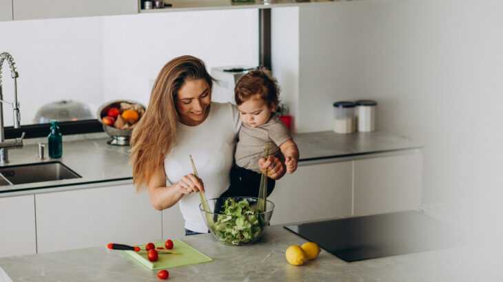 mulher preparando uma salada na cozinha com um bebê no colo
