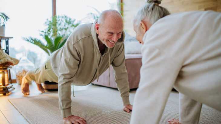 casal de idosos pratica um alongamento dentro de casa