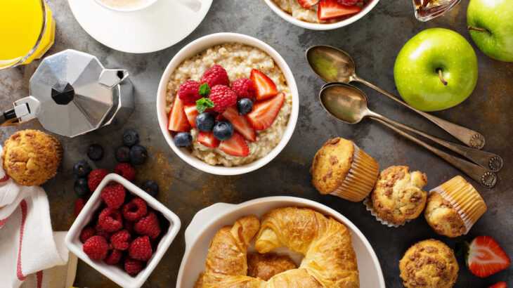 mesa de café da manhã vista de cima com mingau de aveia, pães, muffins, frutas, suco, café e mais