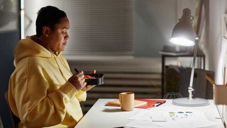 mulher comendo em cima da mesa do escritório à noite