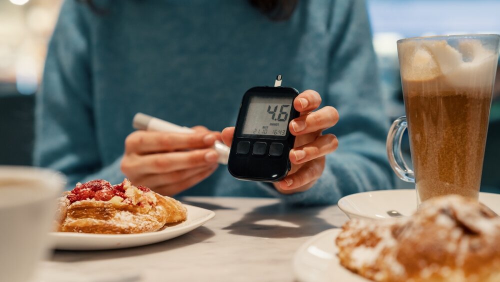 mulher mostrando o glicosímetro em uma mesa com pães e doces