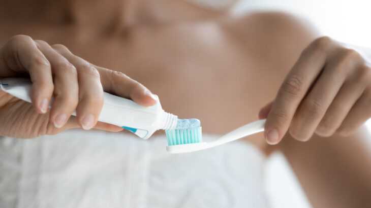 mulher de toalha segurando escova e pasta de dentes