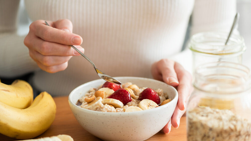mãos femininas segurando uma tigela com aveia e frutas