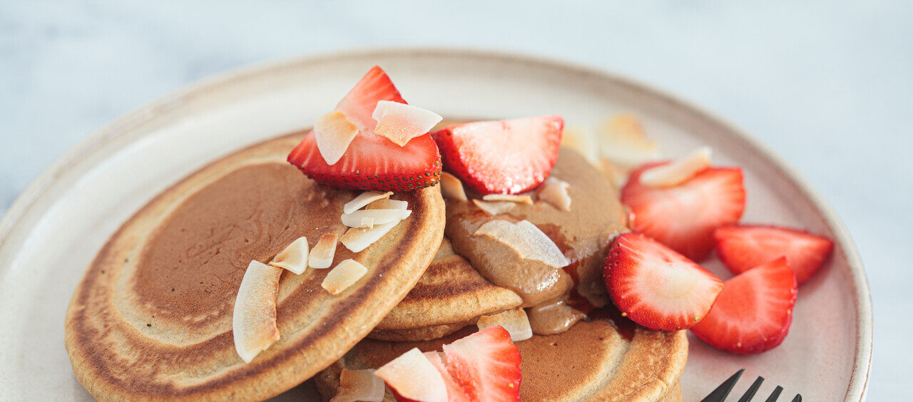 foto de um prato com duas panquecas, morangos picados e amêndoas em lâminas