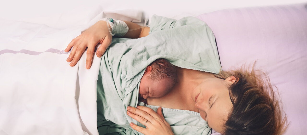 mulher deitada segurando o seu bebê após o parto