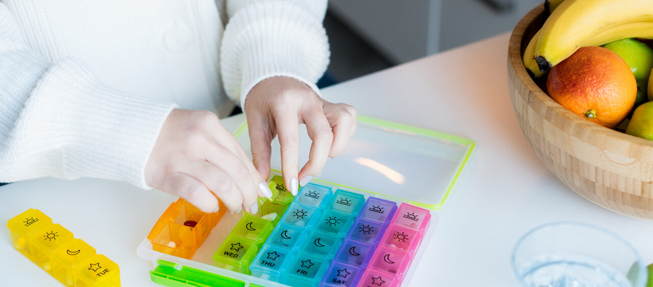 mãos de uma mulher organizando medicamentos em um porta-comprimido