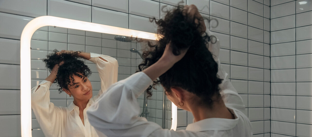 mulher no banheiro prendendo o cabelo em frente ao espelho