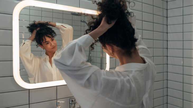mulher no banheiro prendendo o cabelo em frente ao espelho