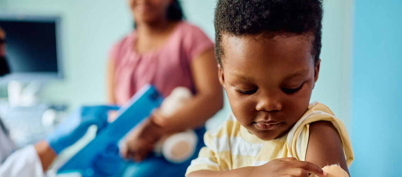 criança apontando para o braço com curativo após tomar uma vacina