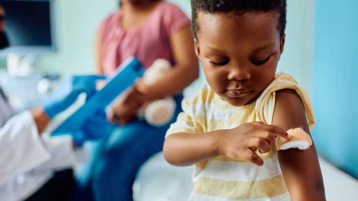 criança apontando para o braço com curativo após tomar uma vacina