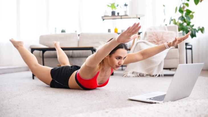 mulher executando o exercício abdominal superman na sala de casa em frente ao computador