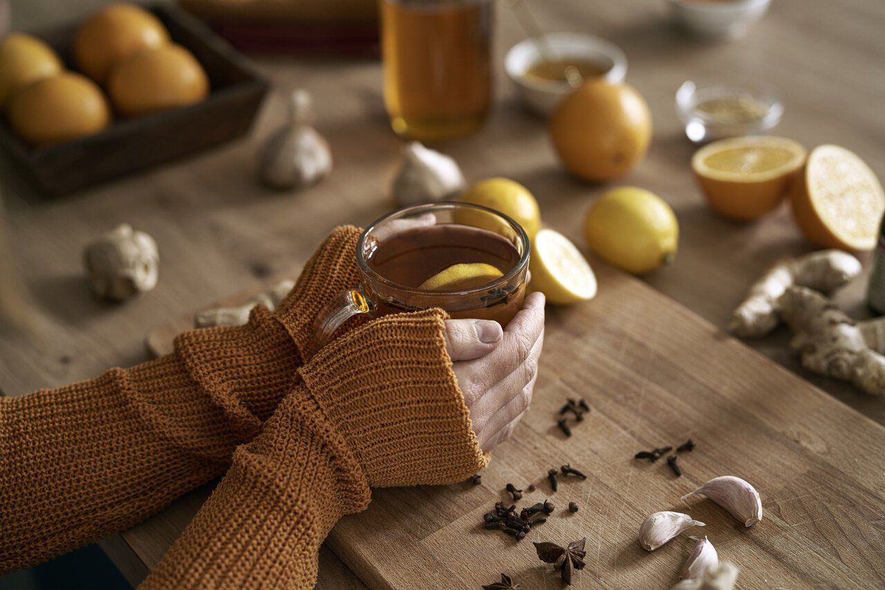 mãos femininas segurando uma xícara de chá com especiarias, mel e limão na mesa 