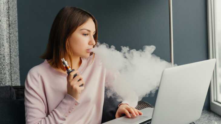 mulher jovem fumando cigarro eletrônico em frente ao notebook