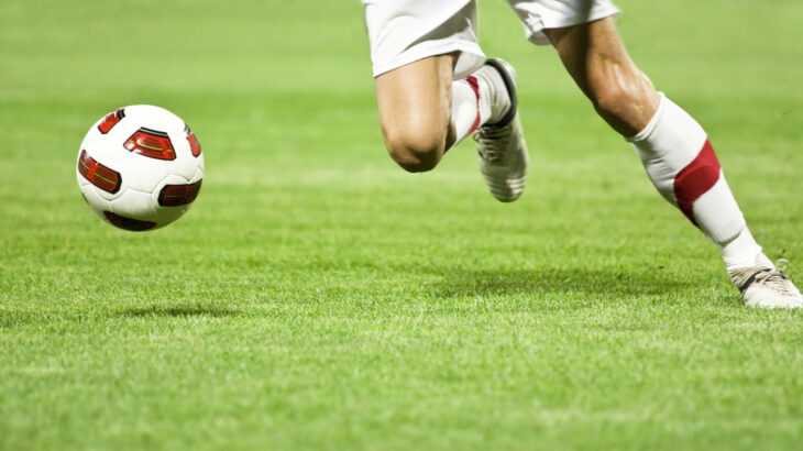 pernas masculinas de um jogador em campo atrás de uma bola