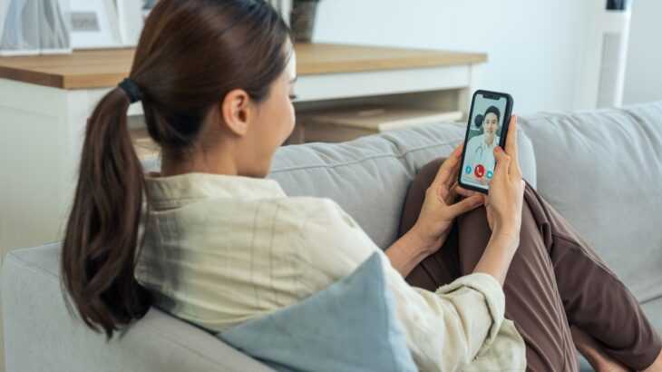 mulher no sofá de casa fazendo uma consulta virtual com um médico