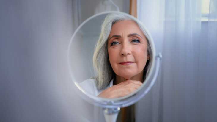 mulher mais velha olhando o seu reflexo em um espelho redondo