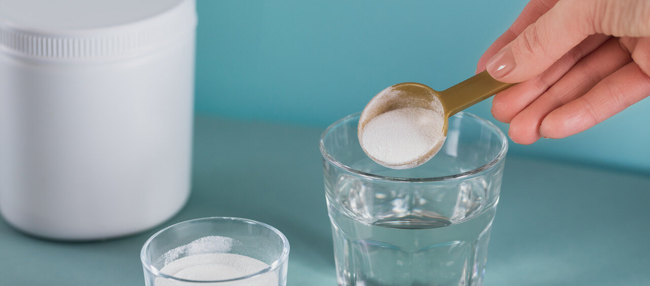 copo com um pó branco dentro e, ao lado, um copo de água com uma mão depositando uma colher desse pó