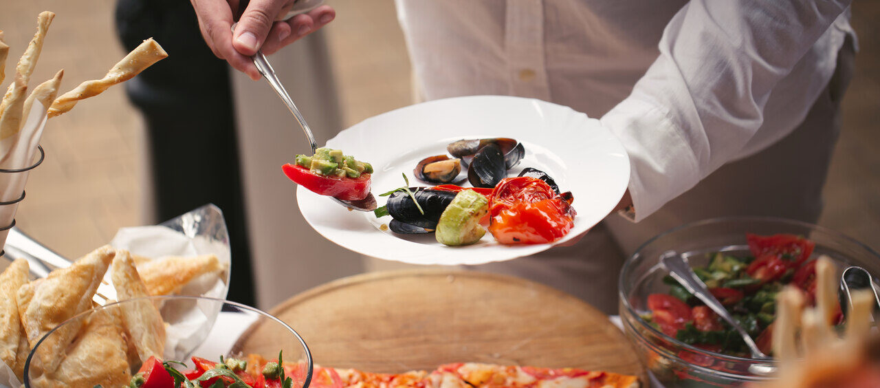 pessoa com um prato na mão pegando comida em um buffet