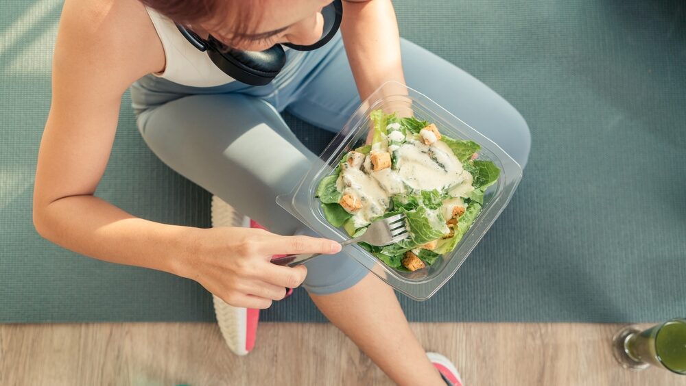 mulher com roupa fitness comendo salada