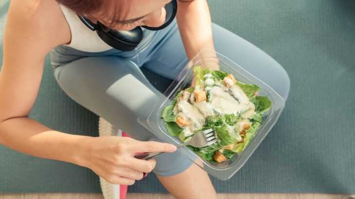 mulher com roupa fitness comendo salada