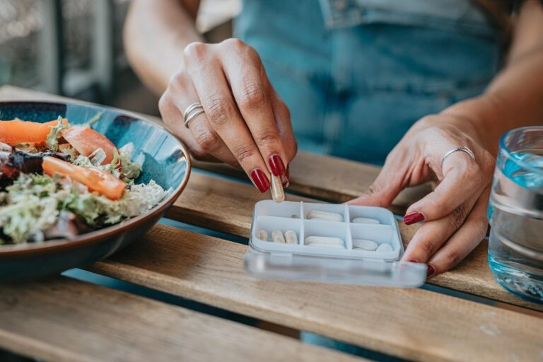 mãos de mulher separando pílulas ao lado de um prato de salada