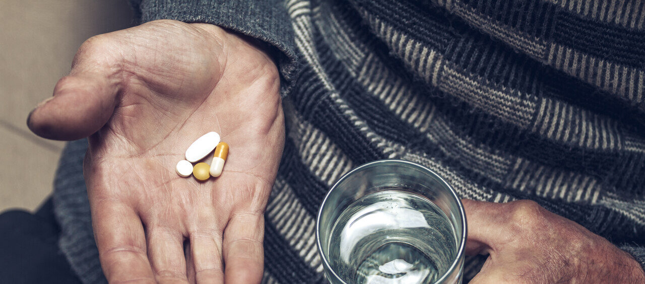 mãos idosas segurando um copo e diversas pílulas