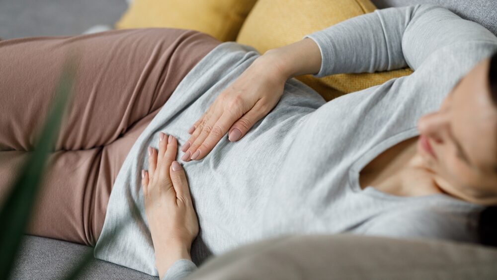 mulher deitada no sofá pressionando o abdômen
