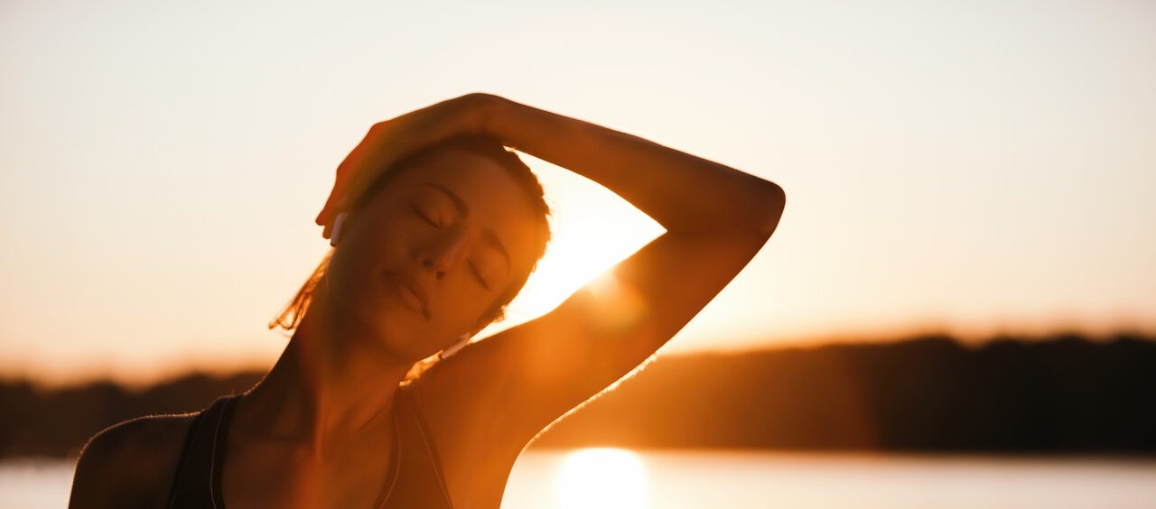 mulher alongando o pescoço na frente de um pôr do sol