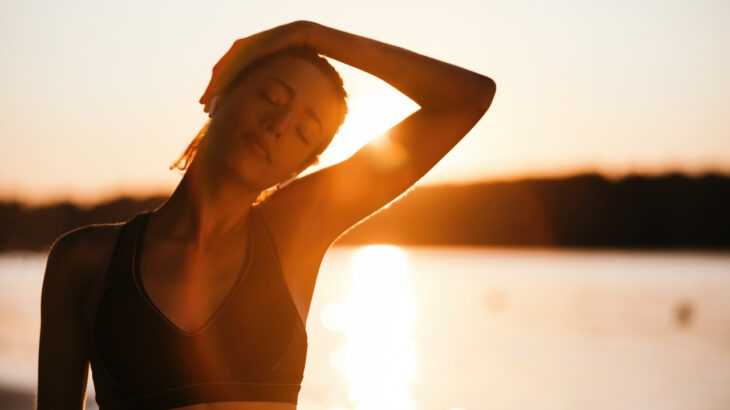 mulher alongando o pescoço na frente de um pôr do sol