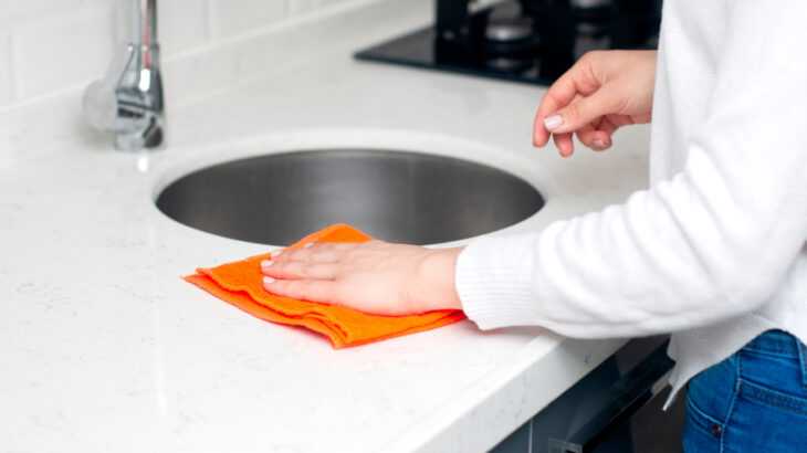 a foto mostra mãos femininas usando um pano de pia para limpar a pia da cozinha