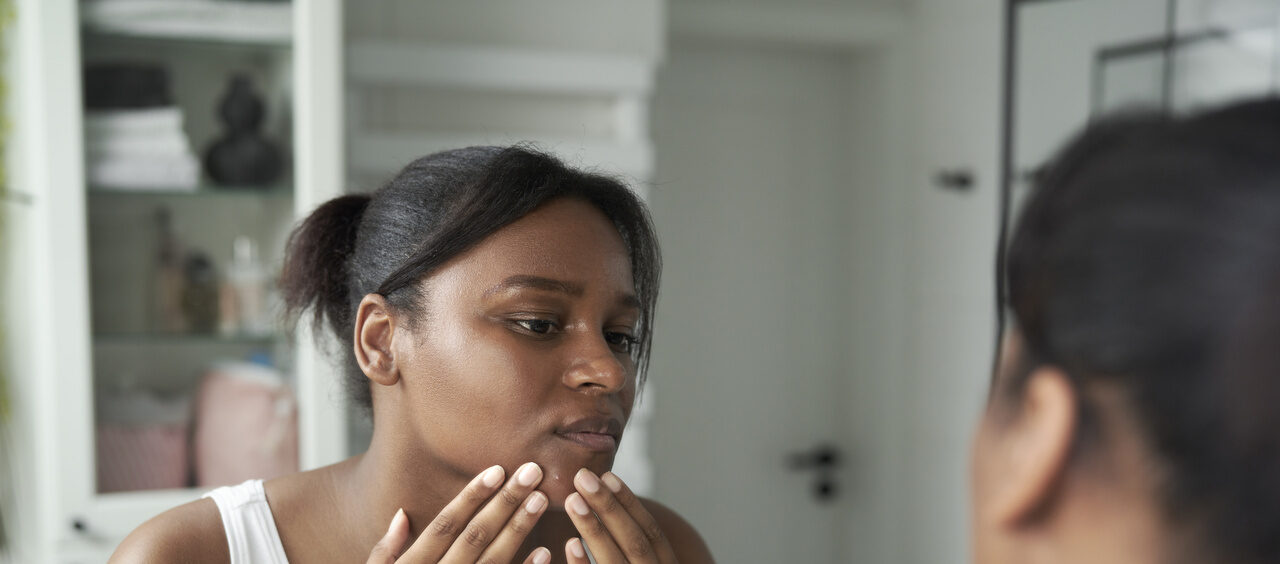 mulher espremendo uma espinha do rosto em frente ao espelho do banheiro
