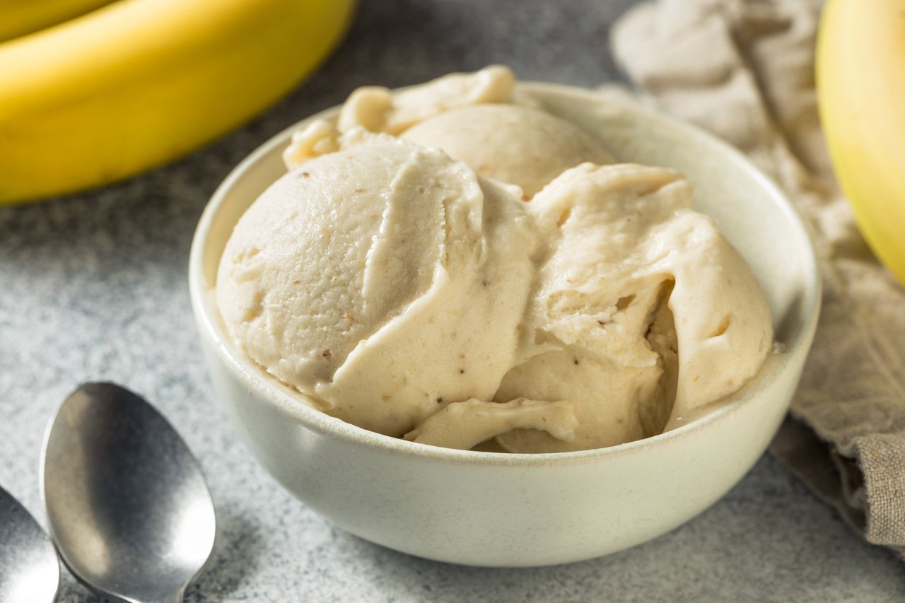 foto de uma cumbuca com sorvete na cor creme. Ao lado, bananas e uma colher