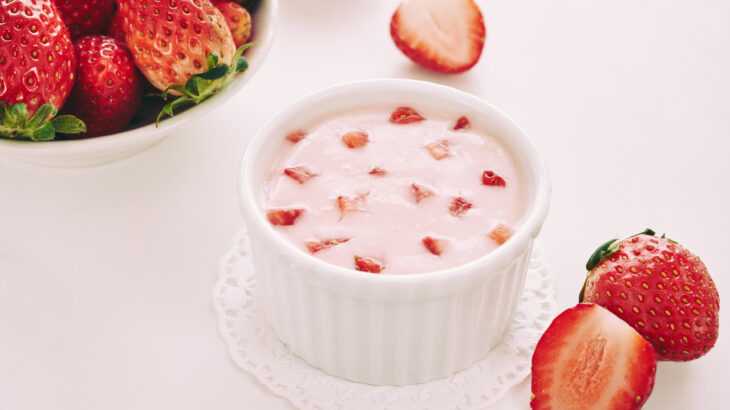 foto de um potinho de cerâmica com um creme rosa enfeitado com pedaços de morango dentro. Ao lato, um pode com morangos