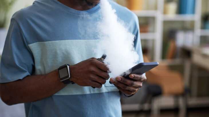 jovem fumando cigarro eletrônico e mexendo no celular