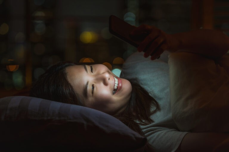 mulher deitada na cama à noite mexendo no celular