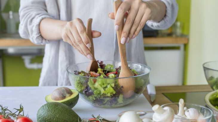 mãos de mulher na cozinha mexendo em uma cumbuca de salada