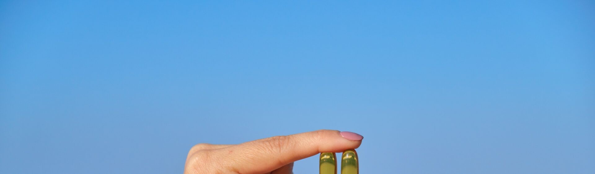mão segurando duas pílulas transparentes contra o sol e em frente ao mar