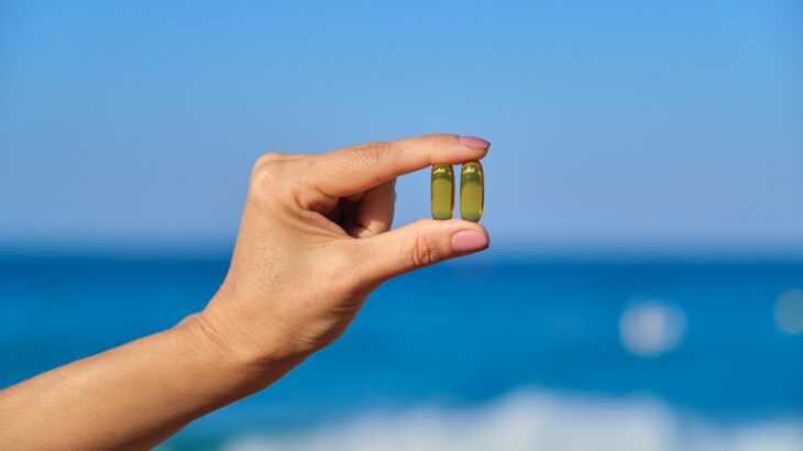 mão segurando duas pílulas transparentes contra o sol e em frente ao mar
