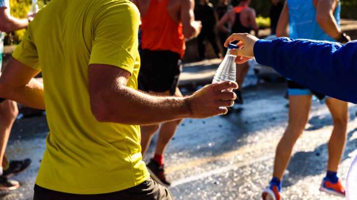 um corredor recebendo uma garrafa de água em uma prova de corrida
