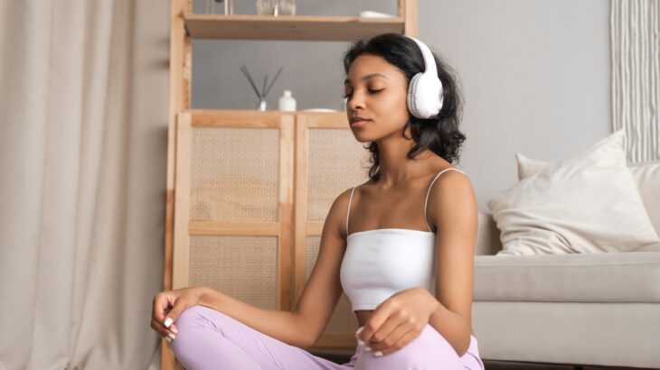 mulher sentada no chão do quarto com um fone de ouvido meditando