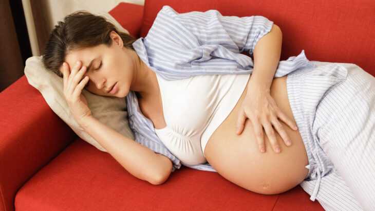 mulher grávida deitada no sofá com dor de cabeça